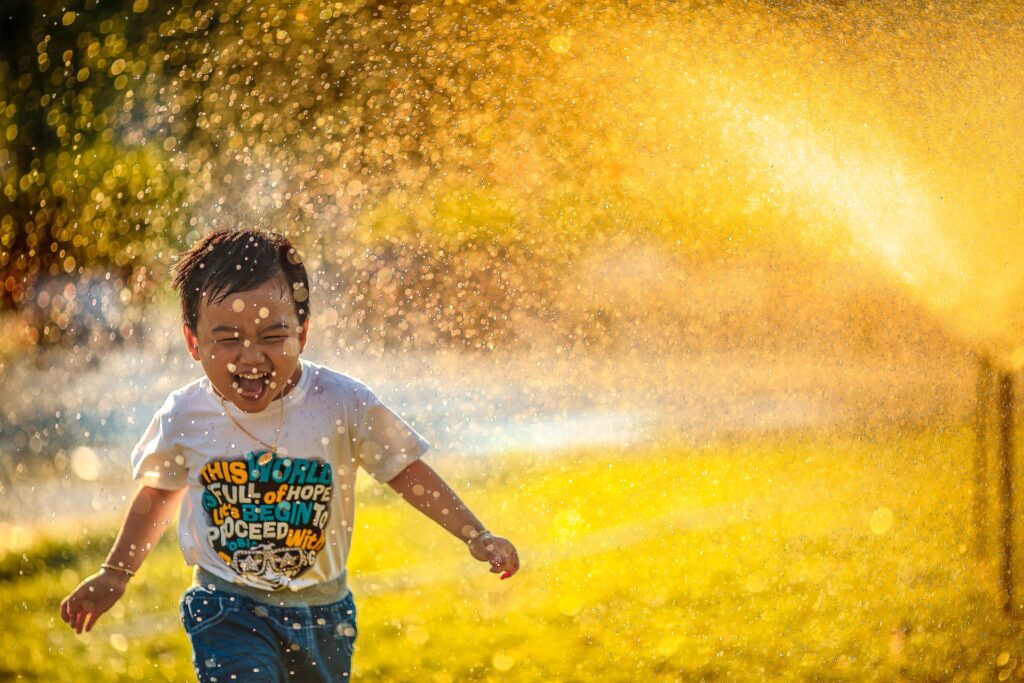 Vitamin A: Junge, der lachend durch Sprühwasser rennt
