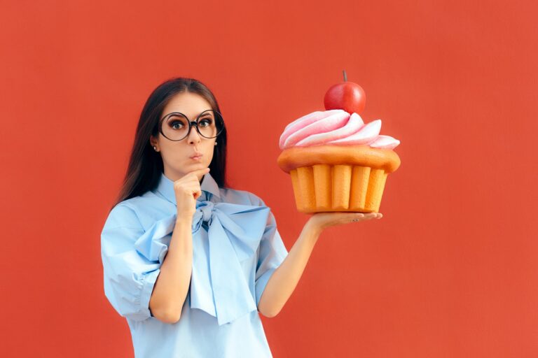 Frau mit fragendem Gesicht, die einen riesigen Cupcake hält