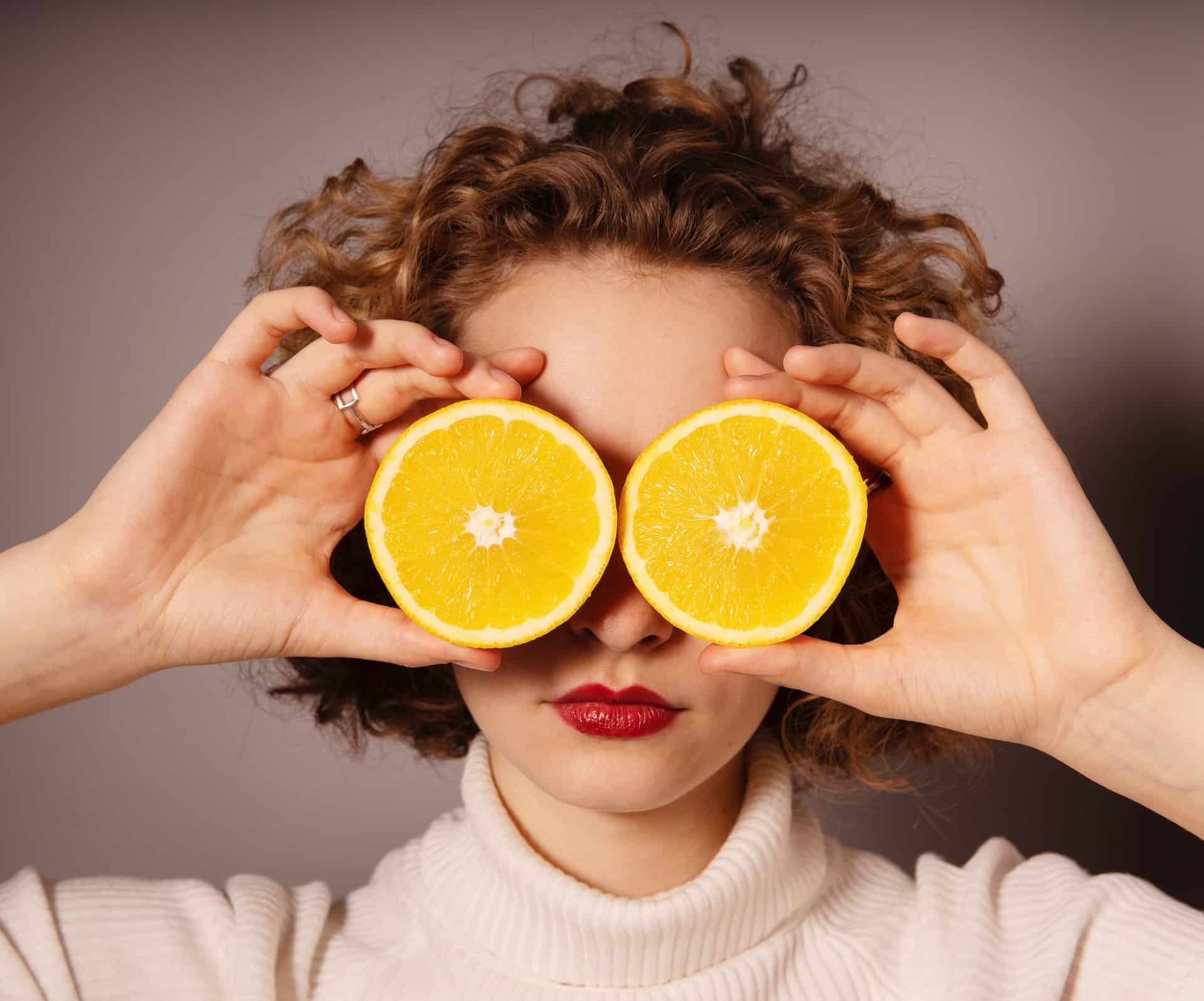 Vitamin-C-Mangel: Frau, die 2 Orangenhälften auf den Augen hat